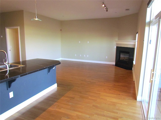 kitchen with baseboards, a fireplace with flush hearth, light wood-style flooring, a kitchen breakfast bar, and a sink