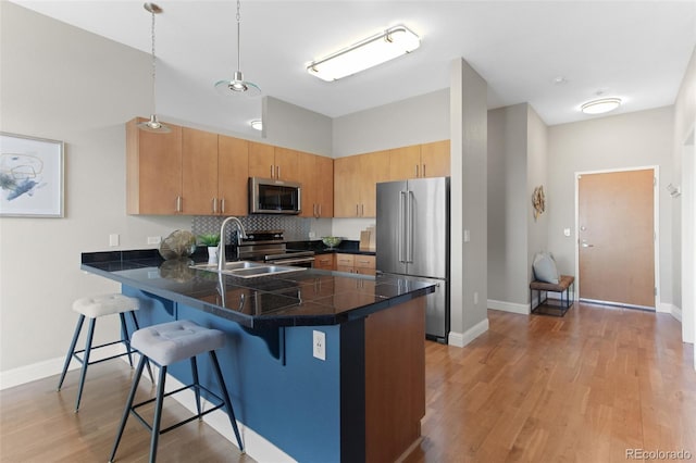 kitchen with light wood finished floors, a sink, a peninsula, appliances with stainless steel finishes, and a breakfast bar area