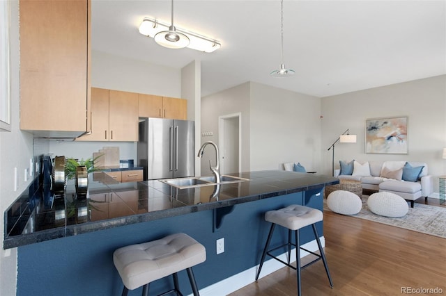 kitchen with light brown cabinets, a sink, high end refrigerator, a peninsula, and a kitchen bar