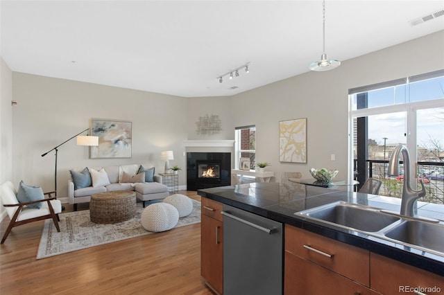 kitchen featuring visible vents, stainless steel dishwasher, a sink, light wood-style floors, and a glass covered fireplace