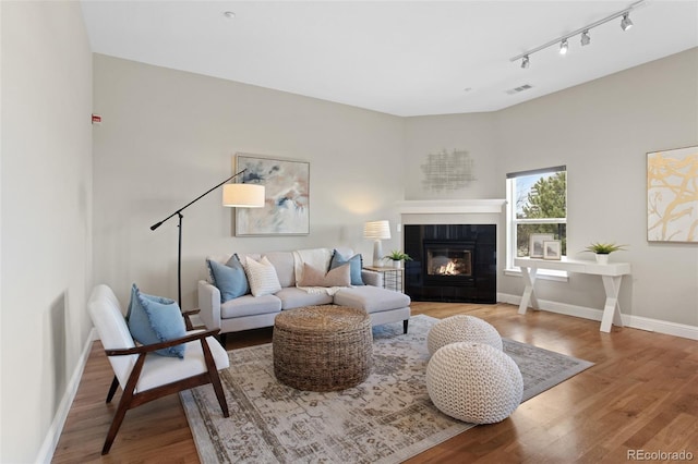 living area with track lighting, wood finished floors, a tile fireplace, and visible vents