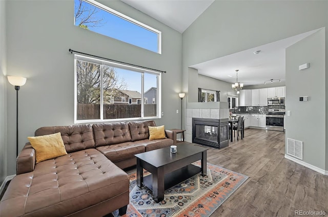 1899 Woodpark Dr, Colorado Springs, CO 80951 - living room with light wood-style floors, a chandelier, high vaulted ceiling, a tiled fireplace, and baseboards
