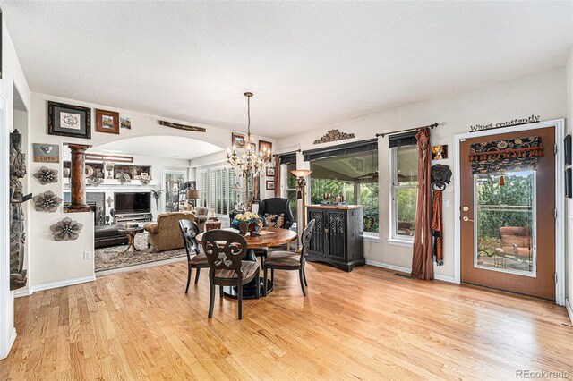 dining room featuring a textured ceiling, light hardwood / wood-style flooring, ornate columns, and a notable chandelier