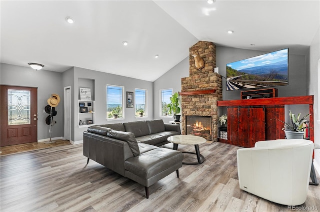 living room with high vaulted ceiling, light hardwood / wood-style floors, and a stone fireplace