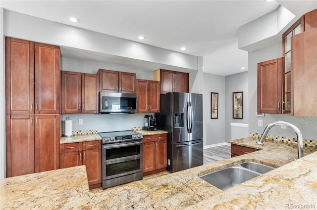 kitchen featuring appliances with stainless steel finishes, sink, light hardwood / wood-style flooring, and light stone countertops