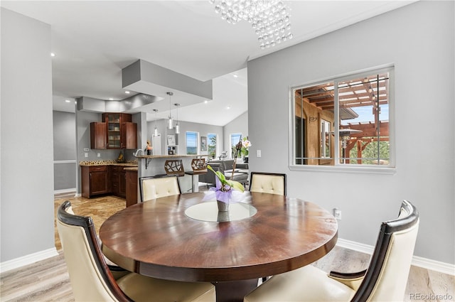 dining space with light hardwood / wood-style floors, vaulted ceiling, and an inviting chandelier