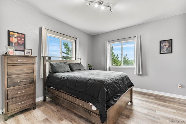 bedroom with light hardwood / wood-style flooring, multiple windows, and track lighting