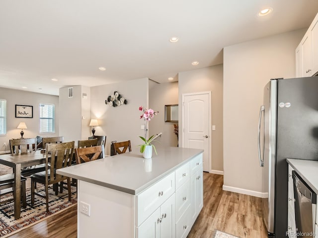 kitchen featuring a center island, light wood-type flooring, appliances with stainless steel finishes, a kitchen breakfast bar, and white cabinets