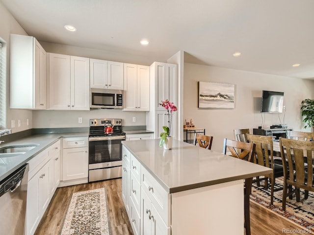 kitchen with white cabinetry, a breakfast bar area, appliances with stainless steel finishes, a center island, and sink