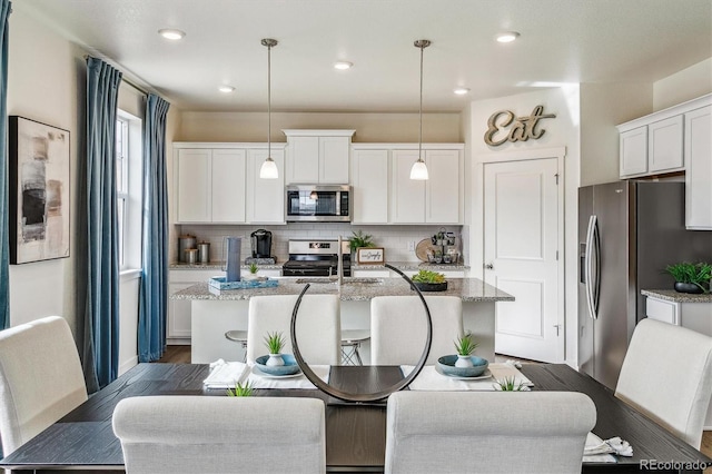 kitchen with pendant lighting, a kitchen island with sink, backsplash, stainless steel appliances, and light stone counters