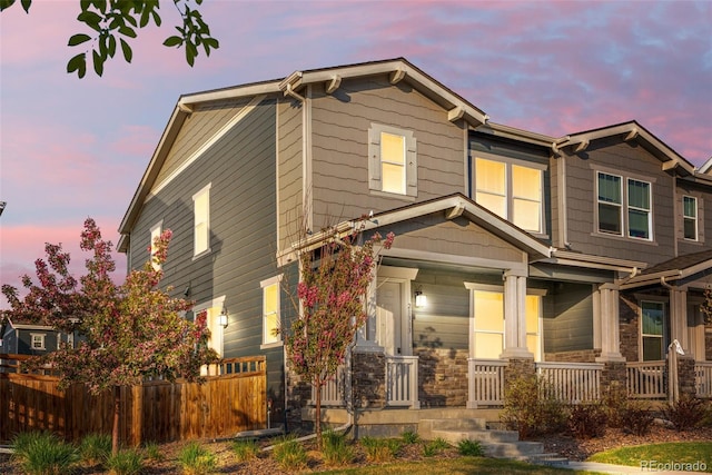 craftsman house with fence, covered porch, and stone siding