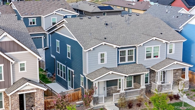 craftsman inspired home with a porch, roof with shingles, cooling unit, fence, and stone siding