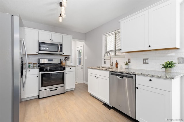 kitchen featuring white cabinets, stainless steel appliances, a sink, tasteful backsplash, and light wood-type flooring