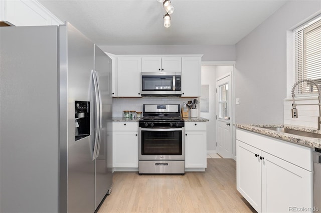 kitchen featuring tasteful backsplash, stainless steel appliances, light wood finished floors, and a sink