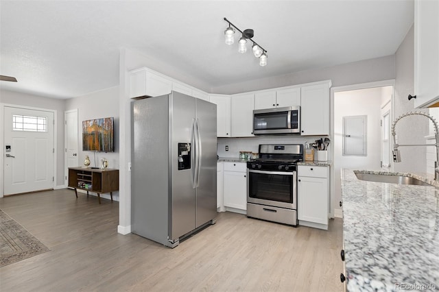 kitchen with appliances with stainless steel finishes, a sink, white cabinetry, and light wood-type flooring