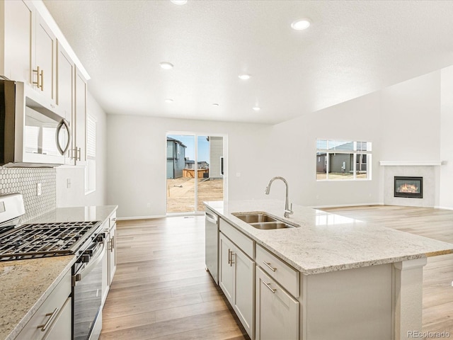 kitchen with an island with sink, stainless steel appliances, plenty of natural light, light stone countertops, and sink