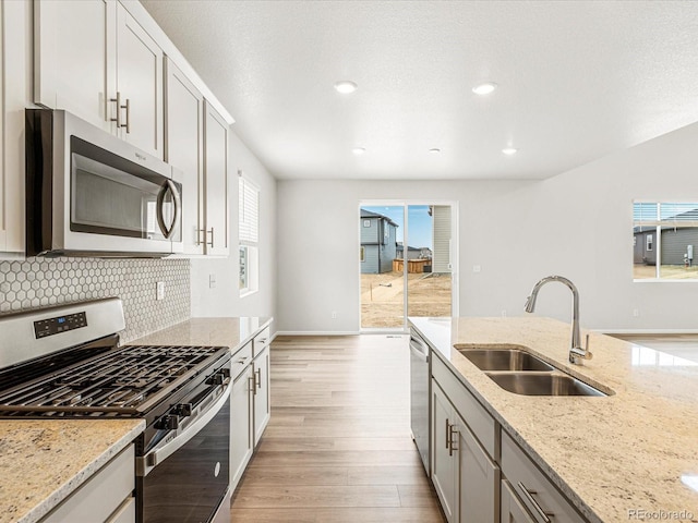 kitchen featuring appliances with stainless steel finishes, backsplash, light wood-type flooring, light stone countertops, and sink