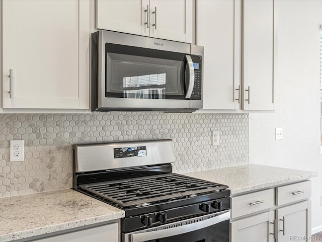 kitchen with appliances with stainless steel finishes, white cabinets, backsplash, and light stone counters