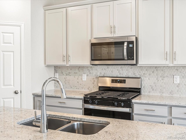 kitchen with tasteful backsplash, sink, light stone countertops, stainless steel appliances, and white cabinets