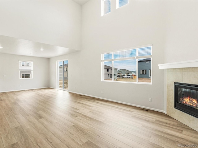 unfurnished living room with a high ceiling, light wood-type flooring, and a fireplace