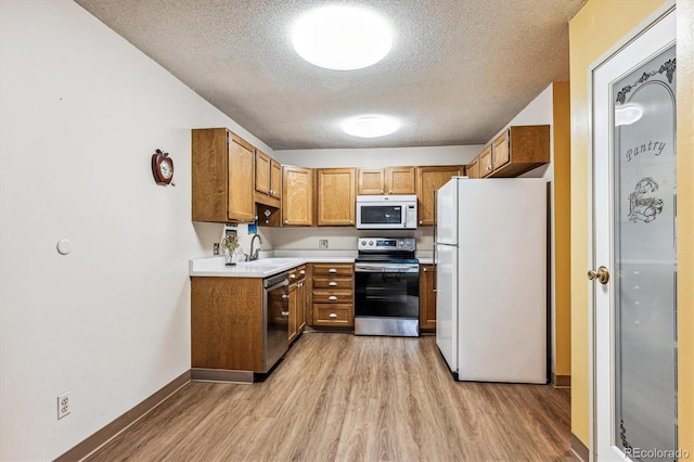 kitchen featuring appliances with stainless steel finishes, a textured ceiling, light wood-type flooring, and sink