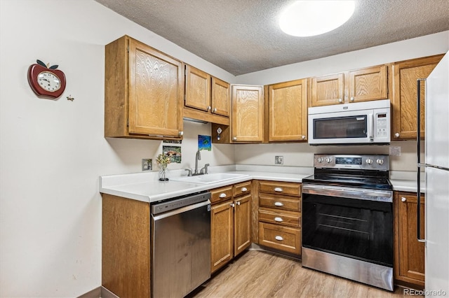 kitchen featuring appliances with stainless steel finishes, a textured ceiling, light wood-type flooring, and sink