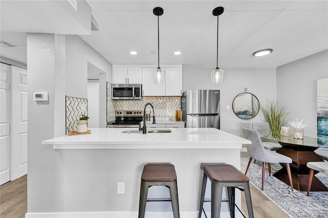 kitchen with a breakfast bar, sink, decorative light fixtures, white cabinetry, and stainless steel appliances