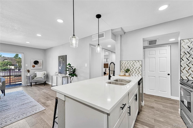 kitchen featuring sink, hanging light fixtures, light hardwood / wood-style flooring, stove, and white cabinets