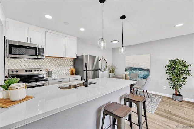 kitchen featuring sink, light hardwood / wood-style floors, decorative light fixtures, white cabinets, and appliances with stainless steel finishes