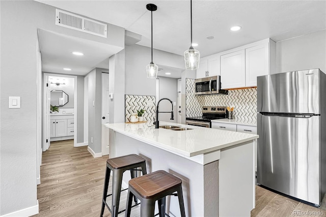 kitchen featuring backsplash, white cabinets, hanging light fixtures, a kitchen bar, and stainless steel appliances