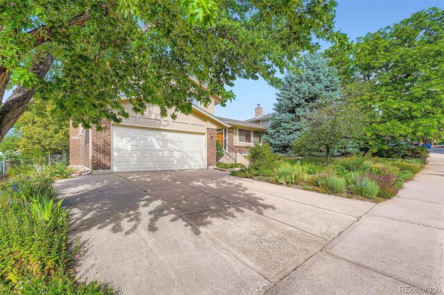 13934 W Warren Dr, Lakewood, CO 80228 - view of property hidden behind natural elements with driveway, a garage, and brick siding