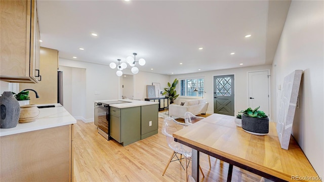 kitchen with sink, electric range oven, light wood-type flooring, green cabinets, and a kitchen island