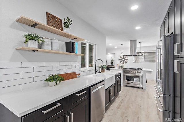 kitchen featuring sink, premium appliances, light hardwood / wood-style flooring, island exhaust hood, and decorative light fixtures