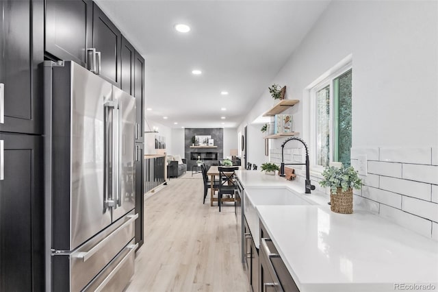 kitchen featuring backsplash, high quality fridge, sink, a fireplace, and light hardwood / wood-style floors