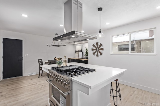 kitchen with stainless steel range, hanging light fixtures, island exhaust hood, a breakfast bar area, and light wood-type flooring