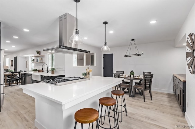 kitchen featuring stainless steel gas stovetop, hanging light fixtures, light wood-type flooring, island range hood, and a breakfast bar area