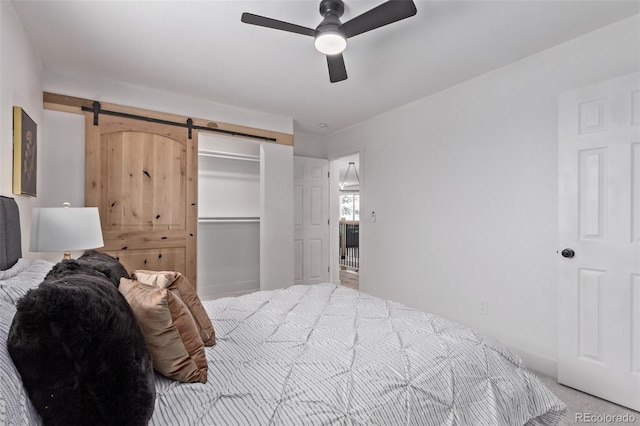 bedroom with a spacious closet, ceiling fan, a barn door, light colored carpet, and a closet