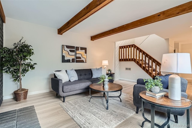 living area featuring beam ceiling, light wood-style floors, stairs, baseboards, and visible vents