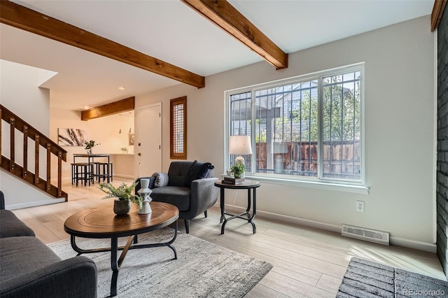 living area featuring visible vents, beam ceiling, baseboards, stairway, and light wood finished floors