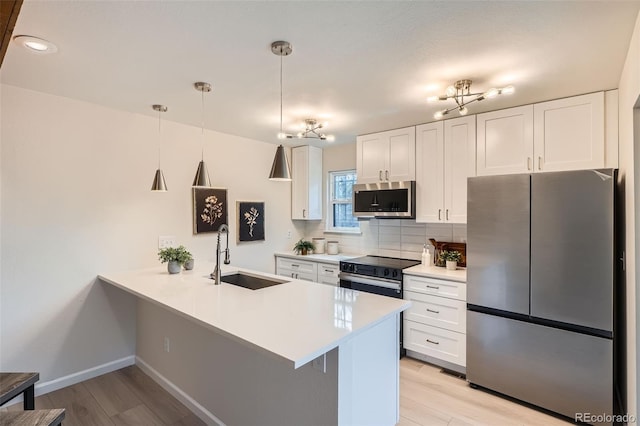 kitchen with appliances with stainless steel finishes, a sink, light wood finished floors, a peninsula, and white cabinetry