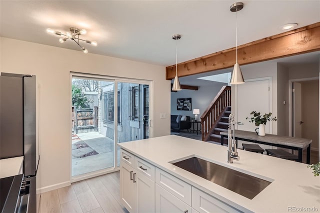 kitchen with hanging light fixtures, a sink, light countertops, freestanding refrigerator, and white cabinetry