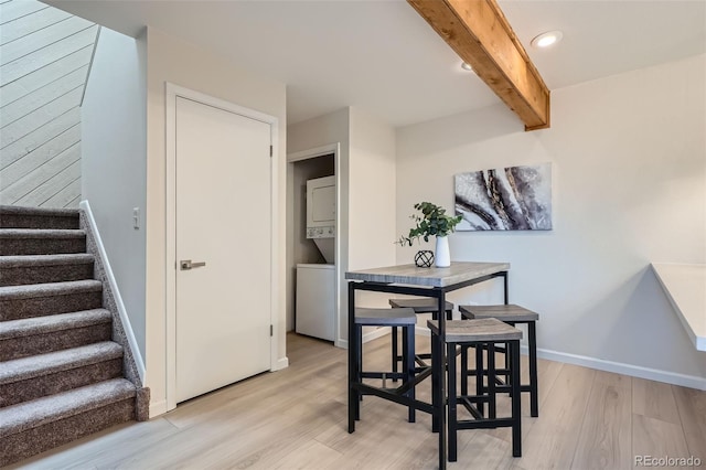 dining area with beam ceiling, light wood finished floors, stacked washing maching and dryer, baseboards, and stairway