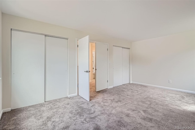 unfurnished bedroom with two closets, carpet flooring, and baseboards