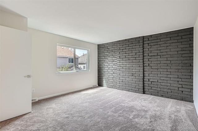 carpeted empty room with brick wall, visible vents, and baseboards