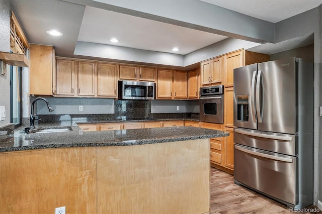 kitchen with appliances with stainless steel finishes, sink, dark stone countertops, kitchen peninsula, and light wood-type flooring