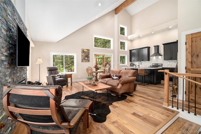 living room featuring high vaulted ceiling, sink, a stone fireplace, and light wood-type flooring