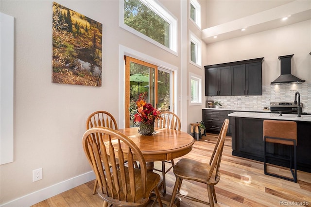 dining room with light hardwood / wood-style flooring, sink, and a towering ceiling