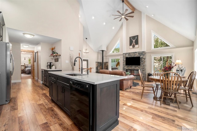 kitchen with black dishwasher, a stone fireplace, light hardwood / wood-style floors, sink, and high vaulted ceiling