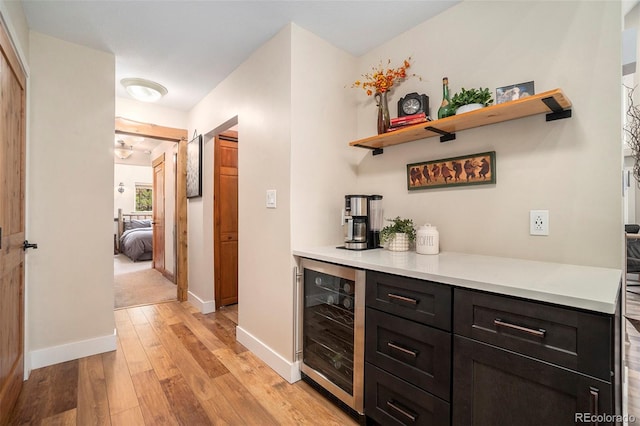 bar with dark brown cabinetry, wine cooler, and light hardwood / wood-style flooring