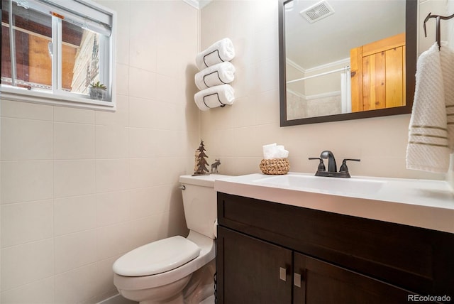 bathroom featuring vanity, toilet, ornamental molding, and tile walls